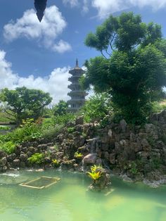 a pond in the middle of a park with rocks and trees around it, under a blue sky with wispy clouds