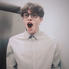 a young man with glasses making a surprised face while standing in front of a refrigerator