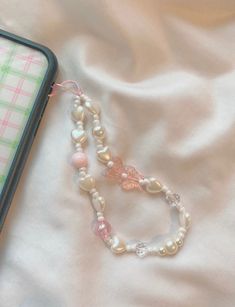 a cell phone is laying next to a necklace on a white sheet with pink and green beads