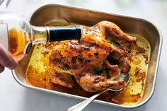 a person is pouring oil on a chicken in a roasting pan with other food