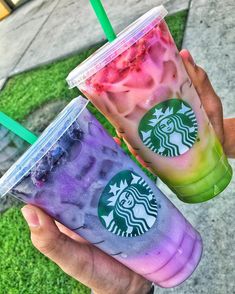 two people holding up starbucks drinks in front of the camera, one is purple and green