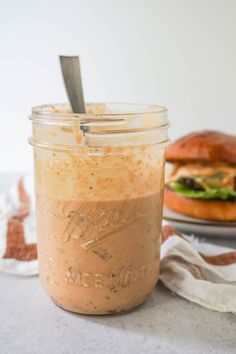 a jar filled with food sitting on top of a table next to a sandwich and napkin