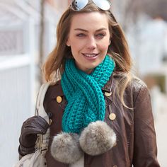 a woman walking down the street wearing a scarf and mittens with pom - poms on it