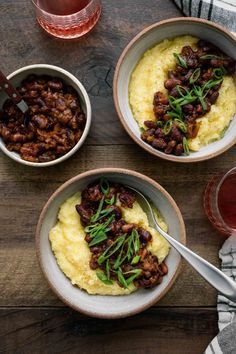 three bowls filled with food on top of a wooden table next to a glass of wine