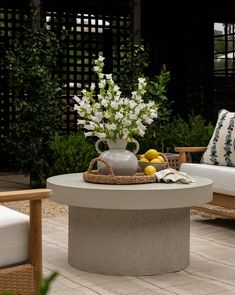 a table with flowers, lemons and a vase on it in the middle of a patio