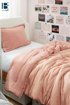 a bed with pink comforter and pillows in a white room next to pictures on the wall