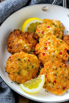 some fried food on a white plate with lemon wedges