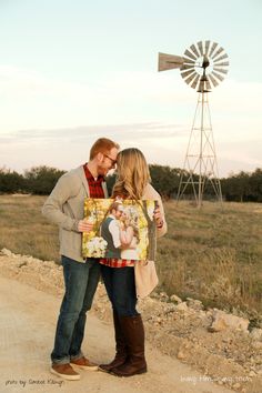 a man and woman standing next to each other on a dirt road with a windmill in the background