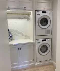 a washer and dryer in a white laundry room with marble counter tops on the wall