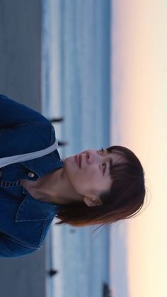 a woman in blue jacket standing next to the ocean with her head tilted back and eyes closed