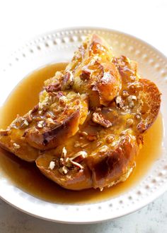 two pieces of bread on a white plate covered in caramel sauce and pecans