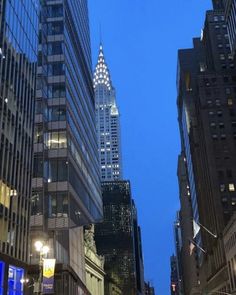 a city street at night with tall buildings in the background and people walking on the sidewalk