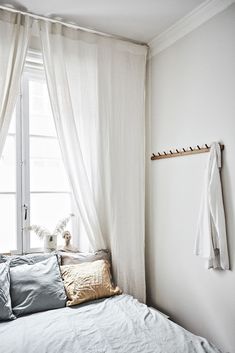 a white bed sitting under a window next to a wooden shelf filled with pillows and blankets