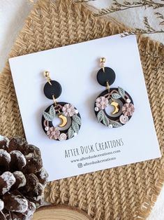 a pair of earrings sitting on top of a piece of paper next to pine cones