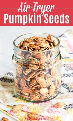 a glass jar filled with pumpkin seeds on top of a floral table cloth and text overlay reads air fryer pumpkin seeds