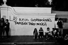 some people are sitting on the sidewalk by a wall with words written in spanish and english