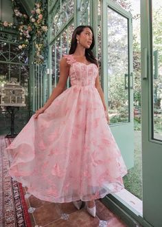 a woman standing in front of a glass door wearing a pink dress