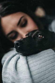 a woman holding a black dog wrapped in a blanket looking at the camera with her eyes closed