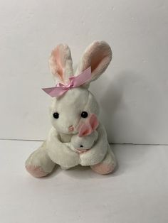 a white stuffed rabbit with a pink bow on its head sitting next to another stuffed animal