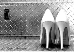 black and white photograph of pair of high heeled shoes in front of metal background