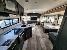 the interior of an rv with wood flooring and black cabinets, windows, and appliances