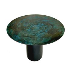 a round metal table with blue and green pattered paint on the top, against a white background