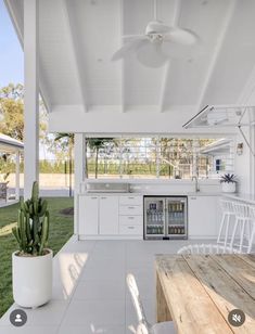 an outdoor kitchen and dining area in a house with white walls, wood floors and ceiling fans