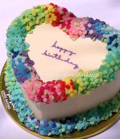 a heart shaped cake with the words happy birthday written on it in purple, blue, green, yellow and pink frosting