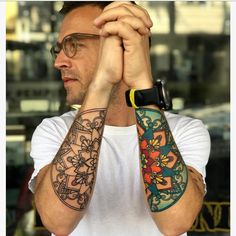 a man holding his hands to his face with tattoos on both arms