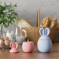 three bunny shaped candles sitting on top of a wooden table next to bread and eggs