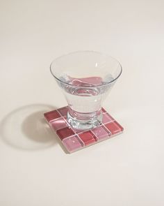 a glass with water in it sitting on top of a tile coaster, against a white background