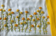 some yellow flowers are on a white table cloth and there is a piece of fabric that has been embroidered onto it