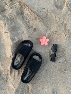 two pairs of black slippers sitting on top of a sandy beach next to a pink flower