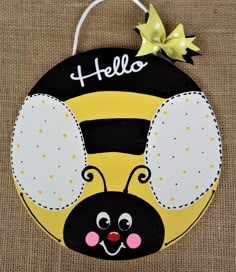 a wooden sign with a bee on it's face and the words hello written in white