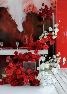 red and white flowers are arranged in front of a large painting on the wall with wine glasses