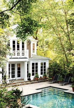 a house with a pool in front of it and trees around the pool area on either side