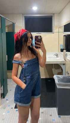 a woman is taking a selfie in the bathroom wearing overalls and a bandana