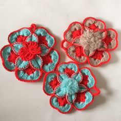 three crocheted flower appliques sitting on a white surface with red and blue petals