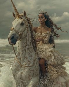 a woman in a dress riding on the back of a white horse near the ocean