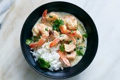 a black bowl filled with rice and shrimp on top of a white countertop next to a spoon