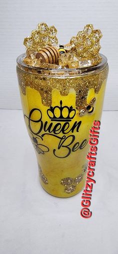 a glass filled with gold glitter next to a white wall and a sign that says queen bee