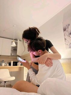 two people sitting on a bed looking at a cell phone in front of their face