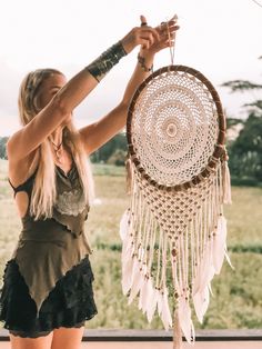 a woman is holding up a white and brown dream catcher