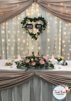 a table topped with flowers and greenery under a heart shaped mr and mrs sign