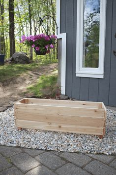 a wooden planter sitting on top of a gravel covered ground next to a house