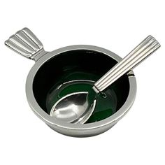 a metal bowl with two spoons in it on a white background, one is green and the other is silver