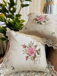 two pillows with pink roses on them sitting next to a potted plant