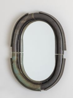 an oval mirror hanging on the wall next to a white wall with a metal frame