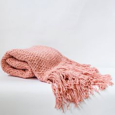 a pink knitted blanket laying on top of a white bed next to a stuffed animal