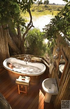 an outdoor bathroom with a tub, sink and toilet in the middle of wood planked flooring